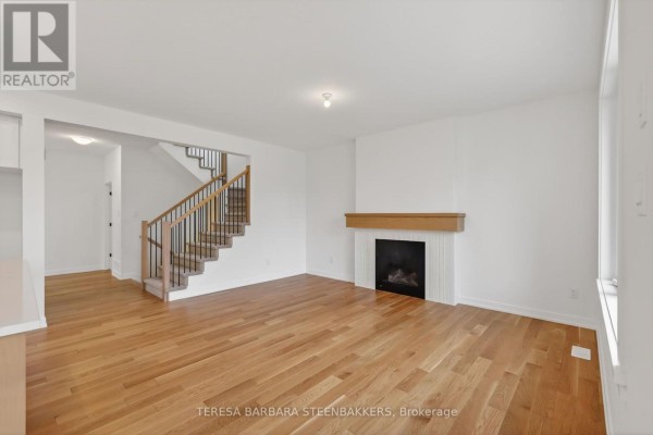 Living room with hardwood floors, fireplace, television, and staircase showing open concept layout. - 1164 Bronze Avenue, Clarence Rockland