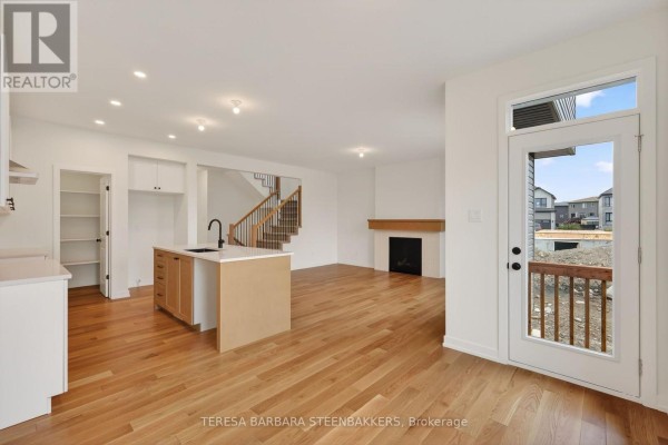 Open concept kitchen and living area with hardwood floors, island, fireplace, and door to outside. - 1164 Bronze Avenue, Clarence Rockland