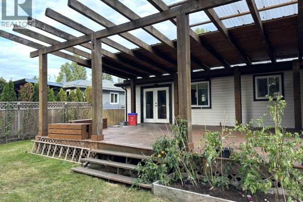 Wooden deck with a covered pergola, double doors, and raised garden beds. - 11645 Steeves Street, Maple Ridge