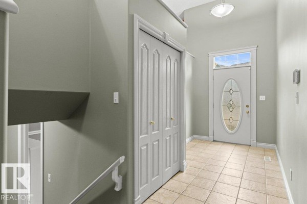 Interior hallway with light green walls, tiled floor, and a wooden staircase. - 11686 15 Av Nw, Edmonton