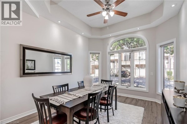 Dining room with a dark wood table, chairs, a large arched window, and a white rug. - 1169 Dorval Drive Unit# 78, Oakville