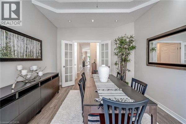 Dining room with a dark wood buffet, table, chairs, and French doors opening to a hallway. - 1169 Dorval Drive Unit# 78, Oakville