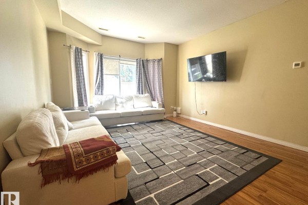 View of the living room from the dining area, featuring a sectional sofa and large rug. - #117 4304 139 Av Nw, Edmonton