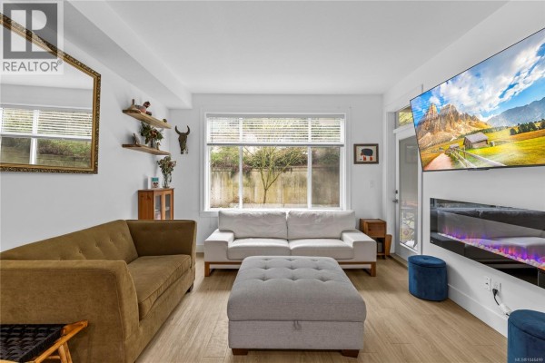 Living room with large window, sectional sofa, and wall-mounted TV. - 117 4960 Songbird Pl, Nanaimo