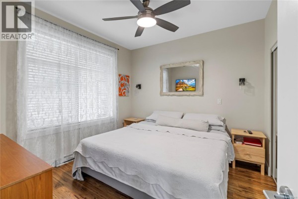 Bedroom with a queen bed, nightstands, and ceiling fan, featuring natural light. - 117 4960 Songbird Pl, Nanaimo