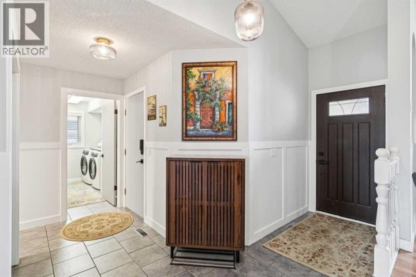 Foyer with tile flooring, a dark wood door, and access to a laundry room with a washer and dryer. - 117 Hawkbury Close Nw, Calgary