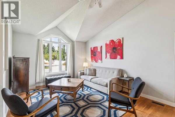 Living room with vaulted ceilings, a large arched window, a sofa, two armchairs, and a coffee table. - 117 Hawkbury Close Nw, Calgary
