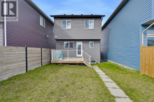 Back exterior of a house with a wooden deck and a grassy backyard. - 117 Howse Avenue Ne, Calgary