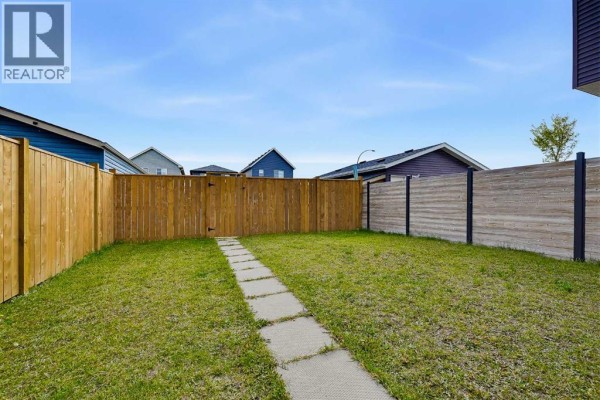 View of a fenced backyard with a stone pathway and wooden gate. - 117 Howse Avenue Ne, Calgary