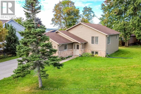 Side view of a beige siding bungalow with a large green lawn and mature trees. - 117 Juneau Road, Tay