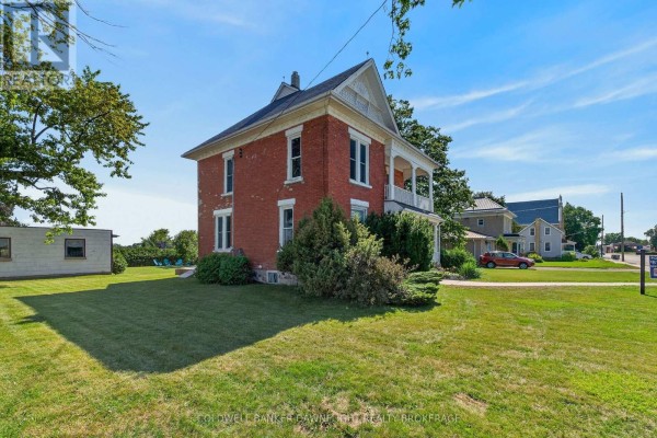Side view of the red brick house showing a large grassy yard and neighboring buildings. - 117 Main Street E, South Huron
