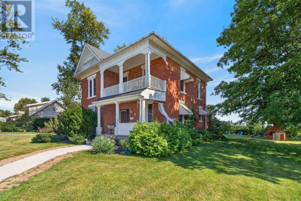 Three-quarter view of the red brick house with a double-decker porch and lush green landscaping. - 117 Main Street E, South Huron