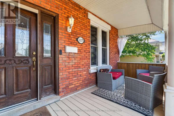 Close-up of the front porch showing a double wooden door, brick exterior, and wicker seating. - 117 Main Street E, South Huron