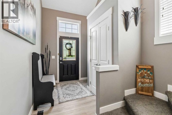 Backyard with green lawn, white vinyl fence, mature trees, and garden beds. - 117 Rainbow Falls Boulevard, Chestermere