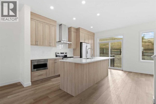 Modern kitchen with light wood cabinets, white countertops, and stainless steel appliances. - 1171 Fowler Road Sw, Airdrie
