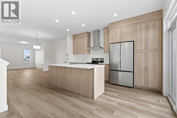 View of a spacious kitchen and living area with light wood finishes and hardwood floors. - 1171 Fowler Road Sw, Airdrie