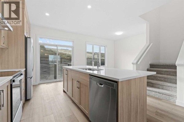 Kitchen island with white quartz countertop, sink, and dishwasher, next to a staircase. - 1171 Fowler Road Sw, Airdrie