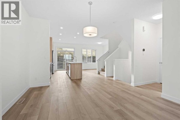 Open-concept living area with a kitchen island, dining area, and staircase to the upper floor. - 1171 Fowler Road Sw, Airdrie