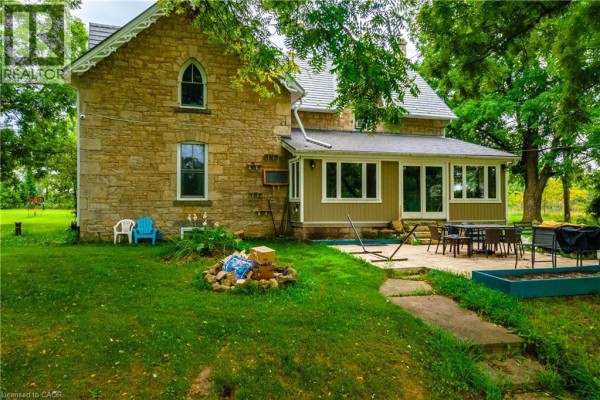 Side view of a stone house showing a patio, lawn, and garden features. - 1172 8th Concession Road W, Flamborough