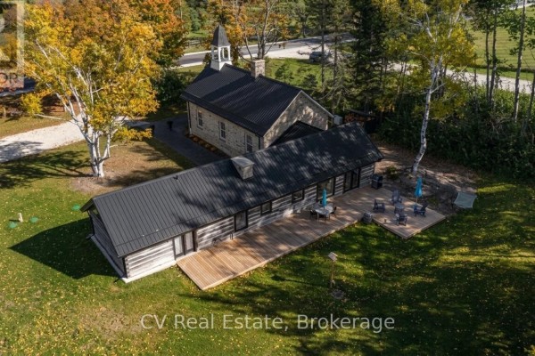 Aerial view of stone church and long log cabin home with wooden decks in green yard. - 1174 10 Nottawasaga Concession, Clearview