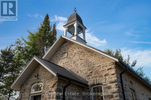 Close-up of stone church facade with arched windows and bell tower against blue sky. - 1174 10 Nottawasaga Concession, Clearview