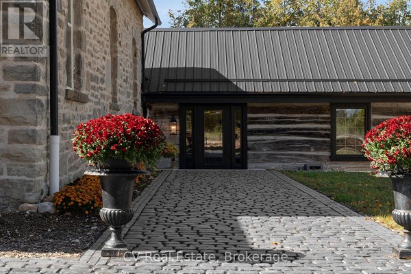 Paved walkway leads to black double doors of log cabin addition, flanked by urns of flowers. - 1174 10 Nottawasaga Concession, Clearview