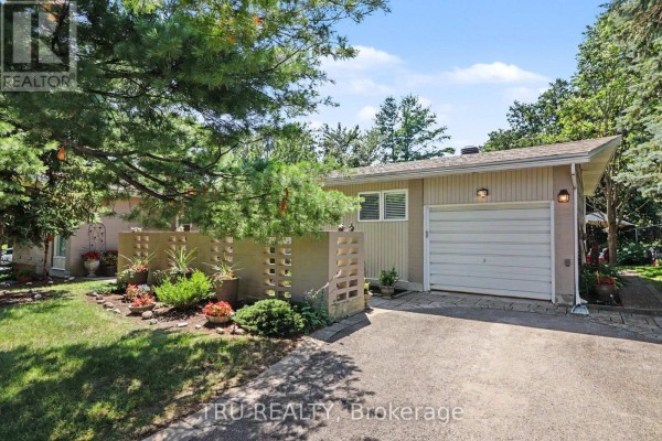 Front exterior of a beige bungalow with a garage door and a decorative concrete block wall. - 1174 Cameo Drive, Ottawa