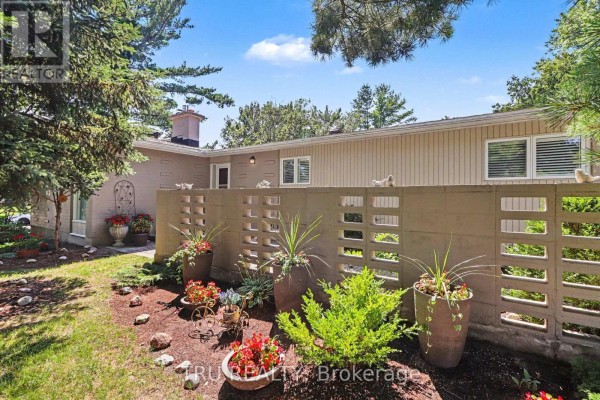 Close-up of a decorative concrete block wall with potted plants and flowers in front of a bungalow. - 1174 Cameo Drive, Ottawa