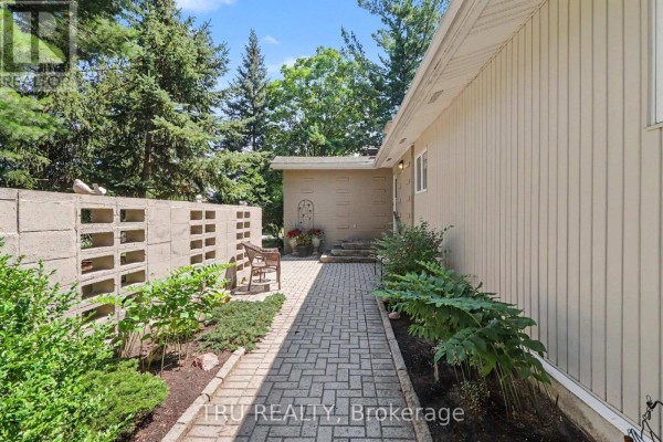 Pathway leading to the side of a beige bungalow with a decorative concrete block wall and landscaping. - 1174 Cameo Drive, Ottawa