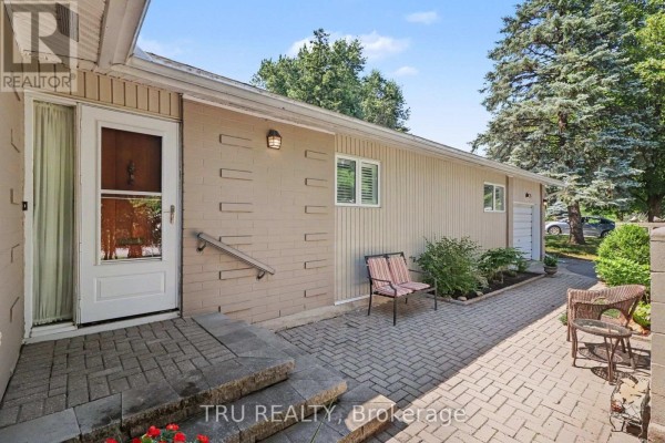 Front entrance of a beige bungalow with a white door, brick accents, and a paved walkway. - 1174 Cameo Drive, Ottawa