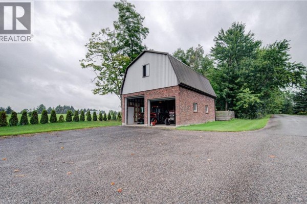 Detached brick building with a metal roof and two garage doors, surrounded by trees. - 1177 Perth Street, New Hamburg