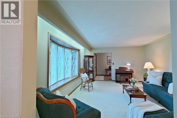 Living room with a large bay window, teal sofa, green chaise lounge, and a upright piano. - 1177 Perth Street, New Hamburg
