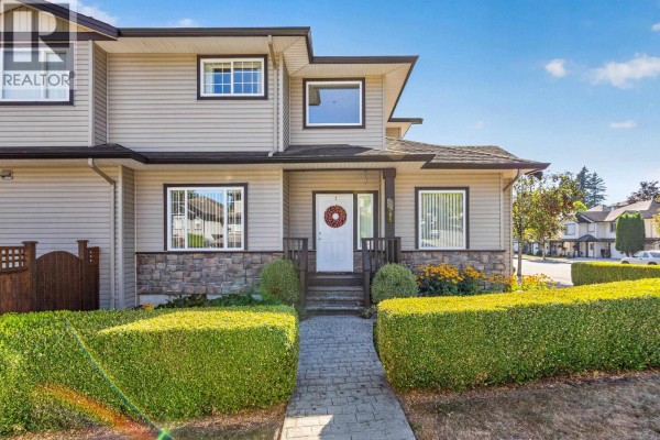 Front entrance of a beige house with a white door, stone base, and neatly trimmed hedges. - 11785 Gilland Loop, Maple Ridge