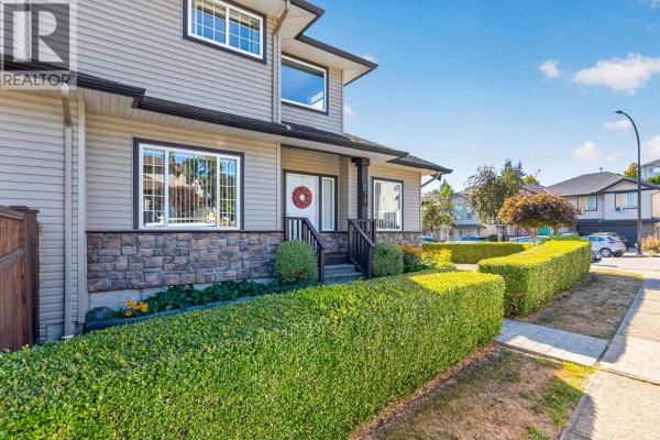 Side exterior view of a two-story beige house with stone accents and green hedges along the sidewalk. - 11785 Gilland Loop, Maple Ridge