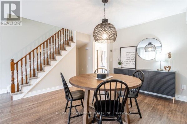 Dining area with staircase, round table, black chairs, and sideboard with artwork. - 118 - 895 Maple Avenue, Burlington
