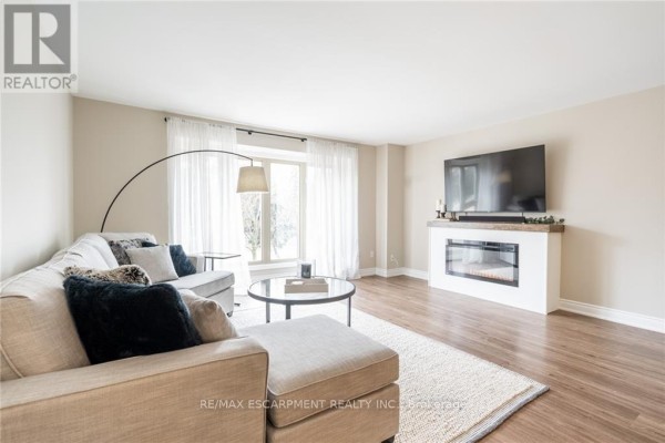 Living room with sectional sofa, coffee table, fireplace, and large window with sheer curtains. - 118 - 895 Maple Avenue, Burlington