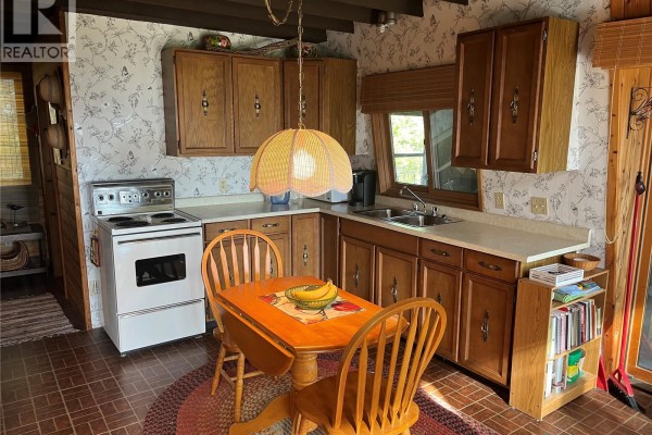 Kitchen with wood cabinets, white stove, sink, and breakfast table. - 118-119 Murray Crescent, Fishing Lake