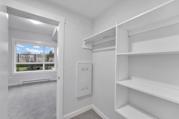 Closet with built-in white shelves and a view of a bedroom with a window. - 118 33886 Pine Street, Abbotsford
