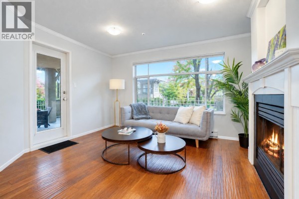 Living room with a gray sofa, coffee tables, fireplace, and large window overlooking trees. - 118 8180 Jones Road, Richmond