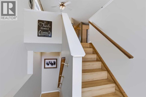 Interior staircase with light oak wood treads, white risers, and a white railing. - 118 Cimarron Grove Crescent, Okotoks