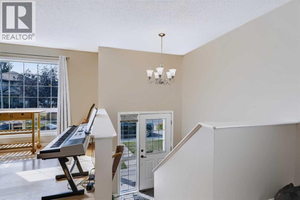Interior view of the main floor showing a piano, a large window with curtains, and the front entrance. - 118 Cimarron Grove Crescent, Okotoks