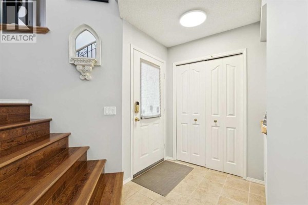 Entrance foyer with a front door, closet doors, a wooden staircase, and tiled floors. - 118 Citadel Crest Park Nw, Calgary