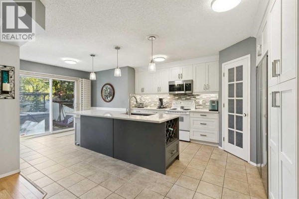 Kitchen with white cabinets, a grey island with a sink, stainless steel appliances, and a sliding glass door. - 118 Citadel Crest Park Nw, Calgary