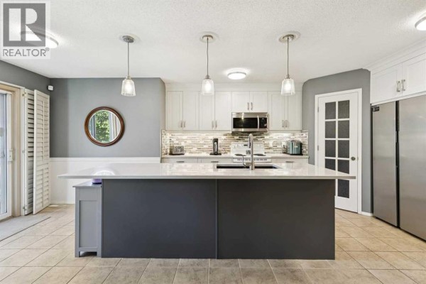 Kitchen with a large grey island, white countertops, white cabinets, and stainless steel appliances. - 118 Citadel Crest Park Nw, Calgary