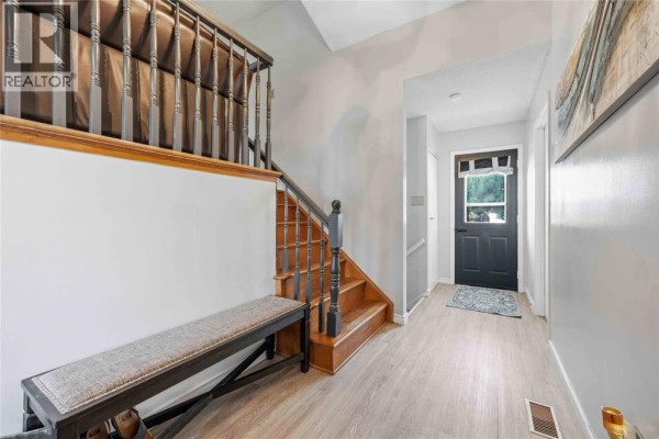 Interior entryway with light grey walls, a dark grey door, and a wooden staircase with a bench. - 118 Finch Drive, Sarnia