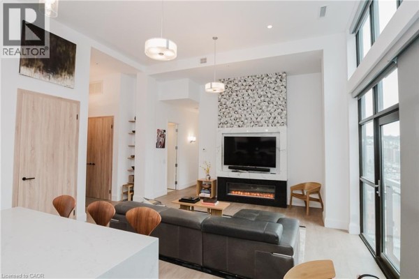 Living room with a fireplace, television, and seating area overlooking the city. - 118 King Street East Unit# Lph13, Hamilton