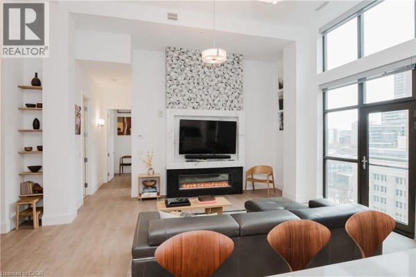 Living room showing a fireplace, television, shelving, and city views through large windows. - 118 King Street East Unit# Lph13, Hamilton