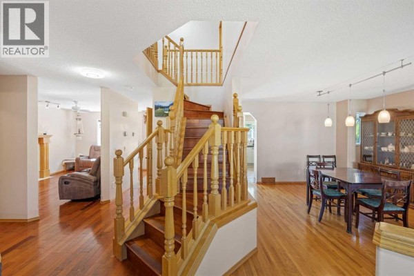 Interior living space with a central wooden staircase, dining area, and visible living room. - 118 Lakeview Shores, Chestermere