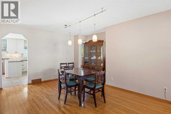 Dining area with a wooden table and chairs, hardwood floors, and a china cabinet. - 118 Lakeview Shores, Chestermere