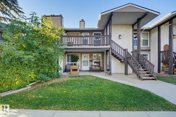Townhouse exterior with a covered staircase leading to an upstairs unit. A small grassy area is in front. - 1180 Saddleback Rd Nw, Edmonton